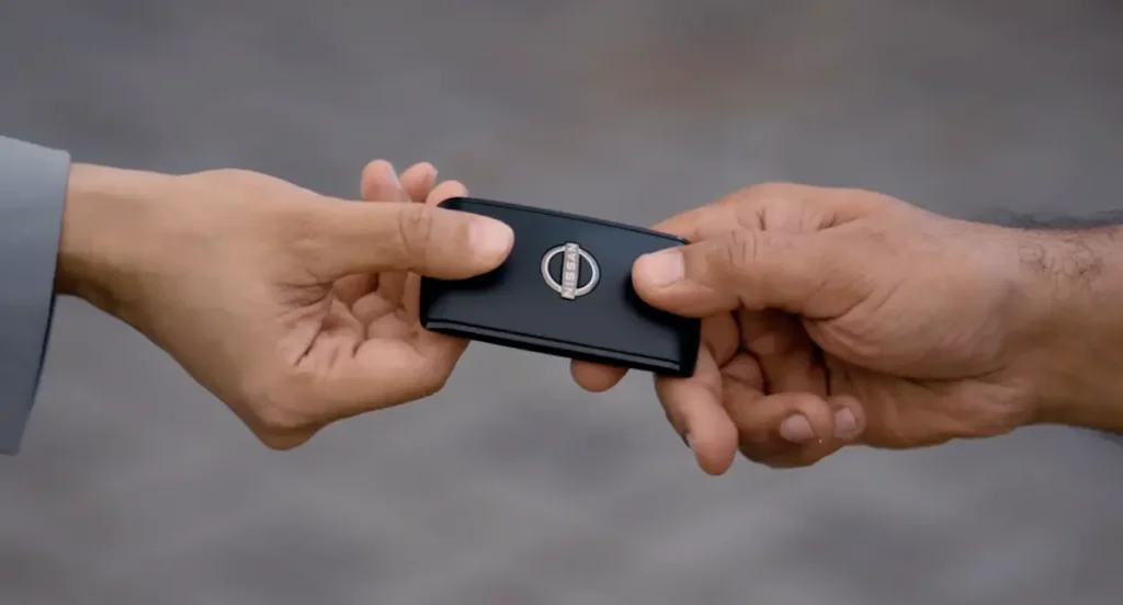 Close-up of two hands exchanging a Nissan-branded smart key fob.