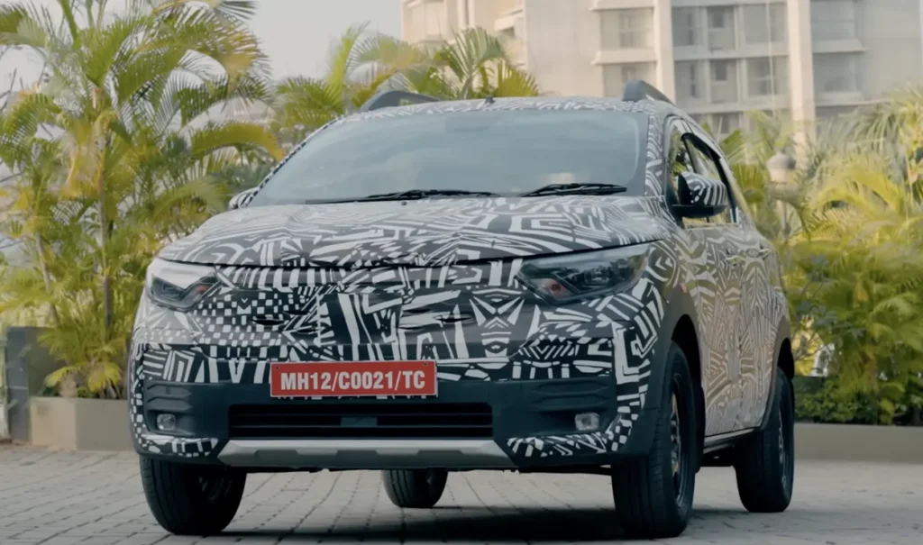 Front view of a camouflaged Nissan Gravite test vehicle parked outdoors with a red temporary test number plate.