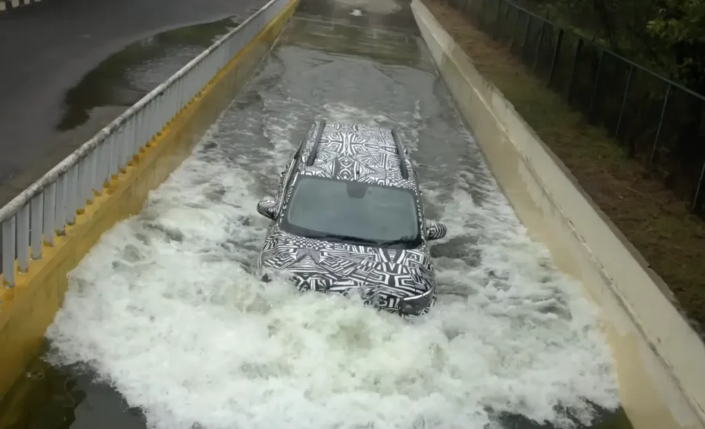Camouflaged Nissan Gravite test vehicle driving through a deep water-wading channel during testing